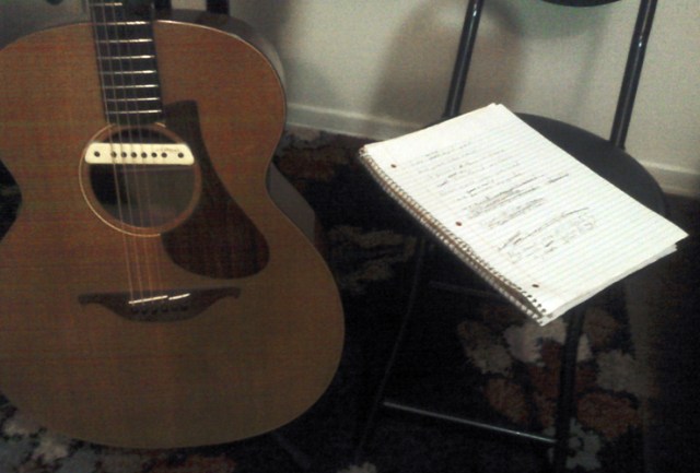My guitar is in my bedroom and I have started writing a new song. The first verse is done and the lyrics are scrawled on that notebook next to my guitar.